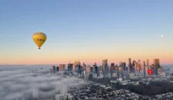Hot air balloons flying over Melbourne with the moon visible at sunrise